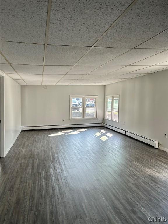 empty room featuring dark wood-style floors, a baseboard radiator, a drop ceiling, and baseboards