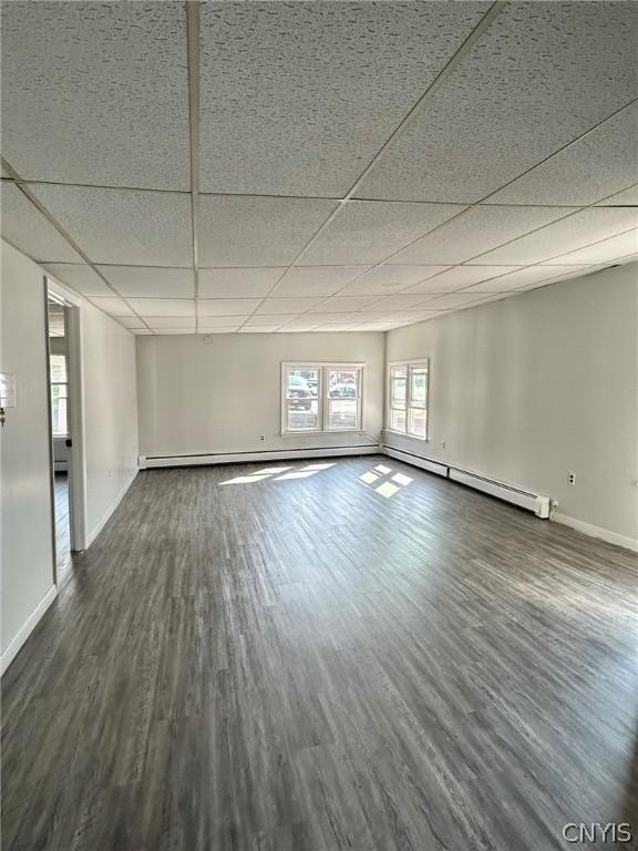 unfurnished room featuring dark hardwood / wood-style flooring, a baseboard radiator, and a drop ceiling