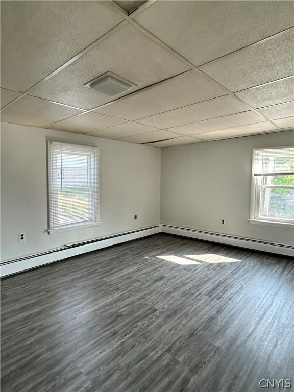 unfurnished room featuring dark hardwood / wood-style flooring, baseboard heating, and a drop ceiling