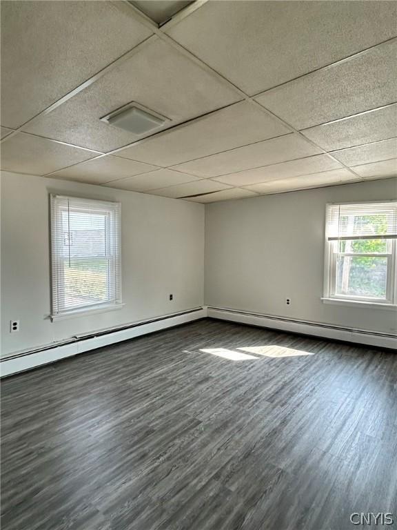 empty room featuring a baseboard heating unit, a drop ceiling, and dark wood-type flooring