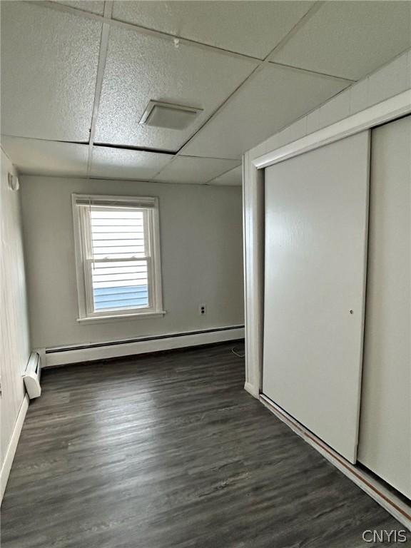 unfurnished bedroom with a closet, a paneled ceiling, and dark hardwood / wood-style flooring