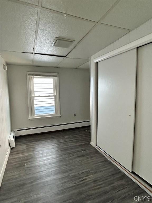 unfurnished bedroom featuring dark wood-style floors, a closet, a baseboard heating unit, and a drop ceiling