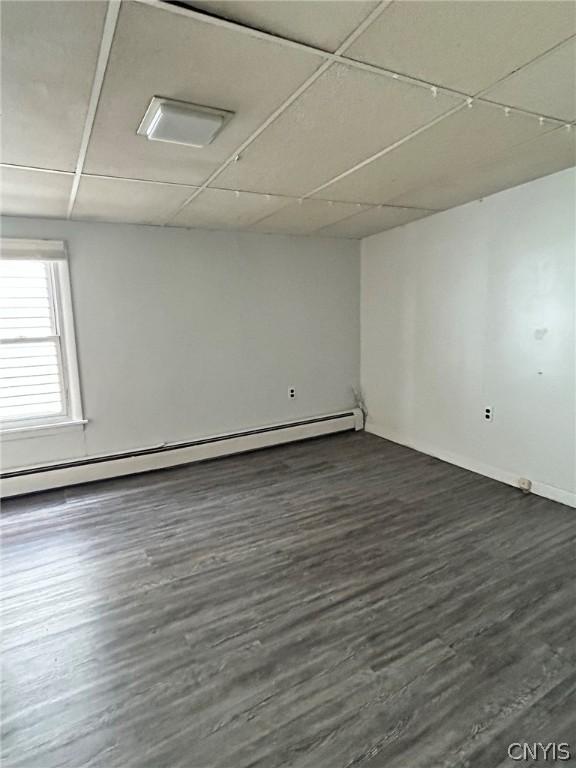 spare room featuring a drop ceiling, a baseboard radiator, and dark hardwood / wood-style flooring