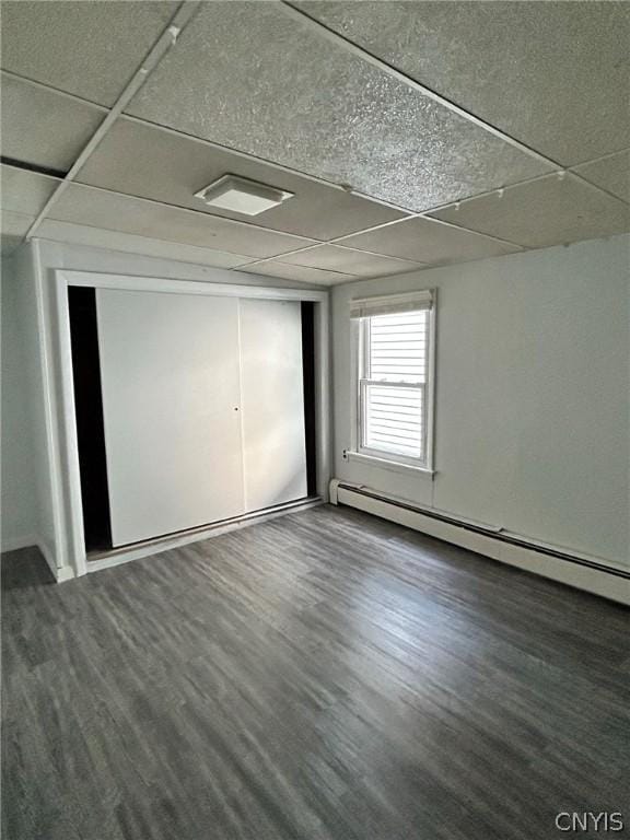 unfurnished bedroom featuring a baseboard heating unit, a paneled ceiling, and wood finished floors