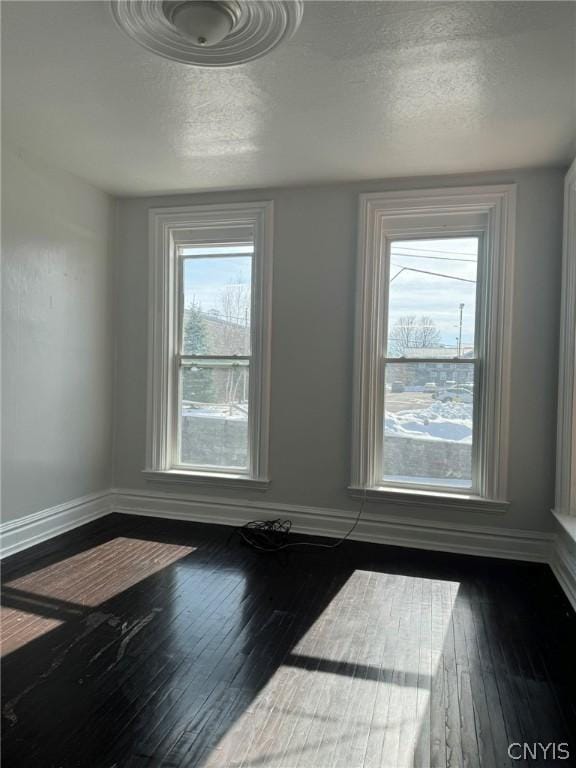 unfurnished dining area with a textured ceiling, dark wood finished floors, and baseboards