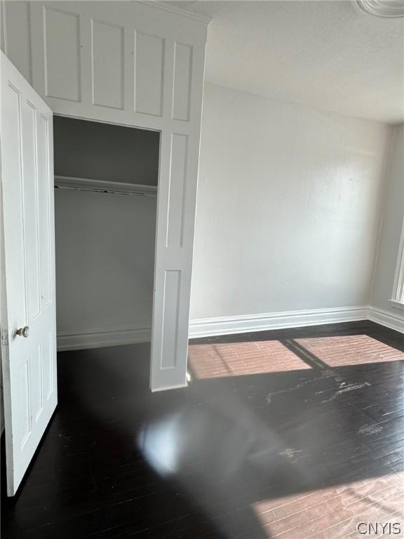 unfurnished bedroom with a closet, wood finished floors, and baseboards