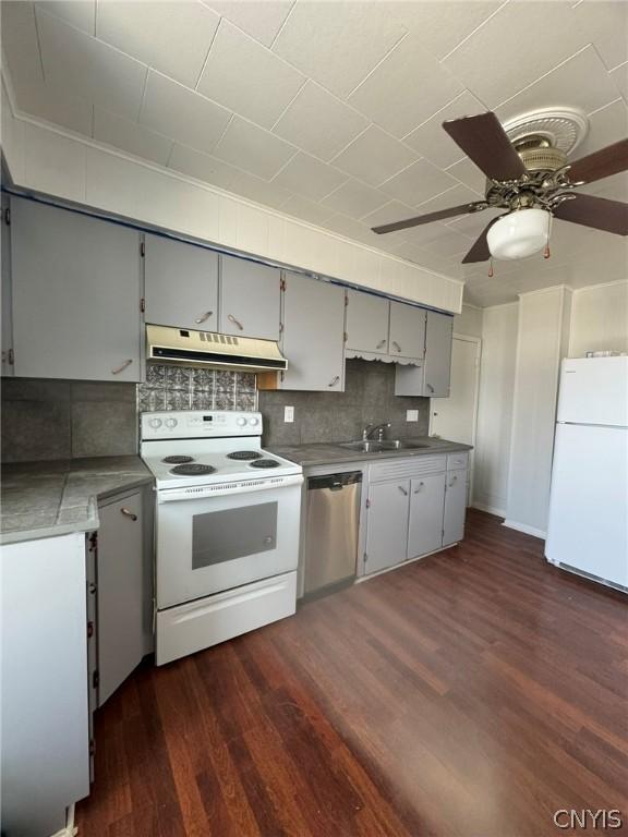 kitchen featuring custom range hood, backsplash, ceiling fan, dark wood-type flooring, and white appliances