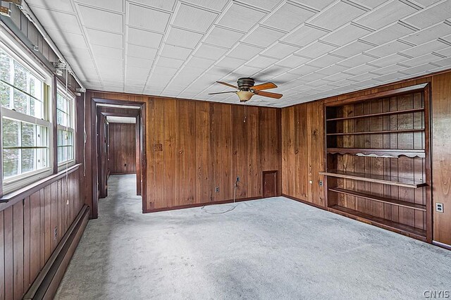 unfurnished room featuring light colored carpet, ceiling fan, a baseboard heating unit, and wood walls