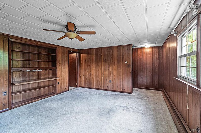 carpeted spare room with built in shelves, wooden walls, and ceiling fan