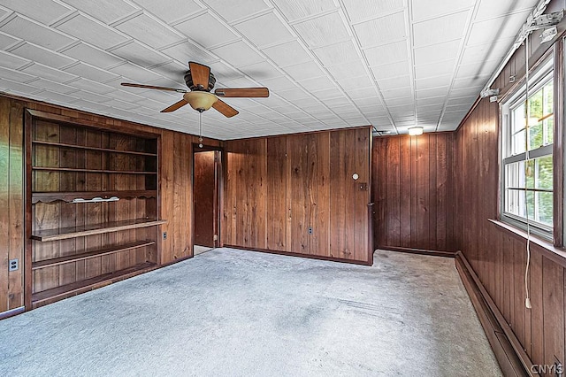 empty room featuring built in shelves, wooden walls, and ceiling fan