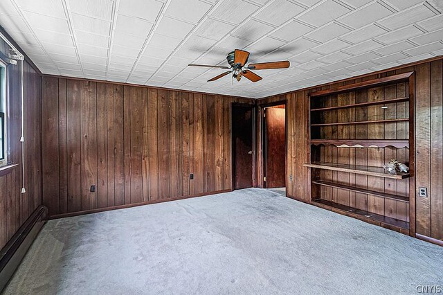 empty room featuring carpet flooring, ceiling fan, wood walls, and baseboard heating