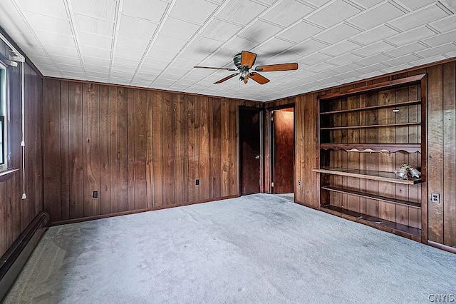 spare room featuring built in features, ceiling fan, carpet flooring, a baseboard radiator, and wood walls