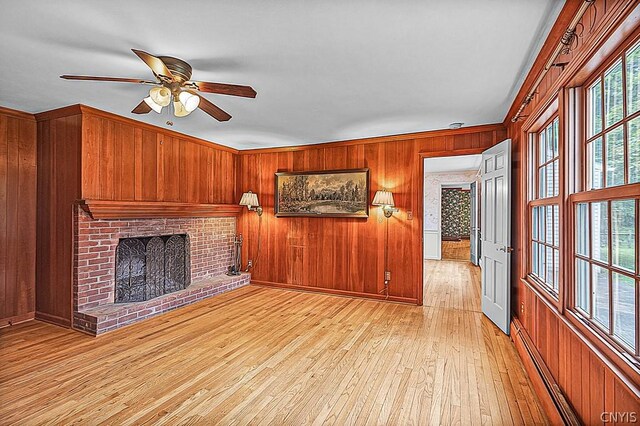 unfurnished living room featuring a fireplace, light hardwood / wood-style floors, crown molding, and wooden walls