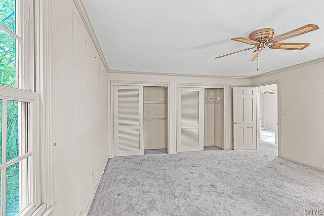 unfurnished bedroom featuring ceiling fan, crown molding, light colored carpet, and two closets