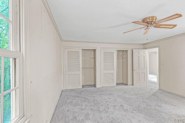 unfurnished bedroom featuring crown molding, two closets, light carpet, and ceiling fan