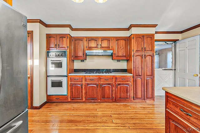 kitchen with light wood-type flooring, ornamental molding, double oven, stainless steel refrigerator, and gas cooktop