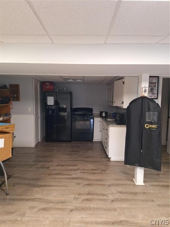 kitchen with black refrigerator with ice dispenser, stove, light hardwood / wood-style floors, a paneled ceiling, and white cabinets