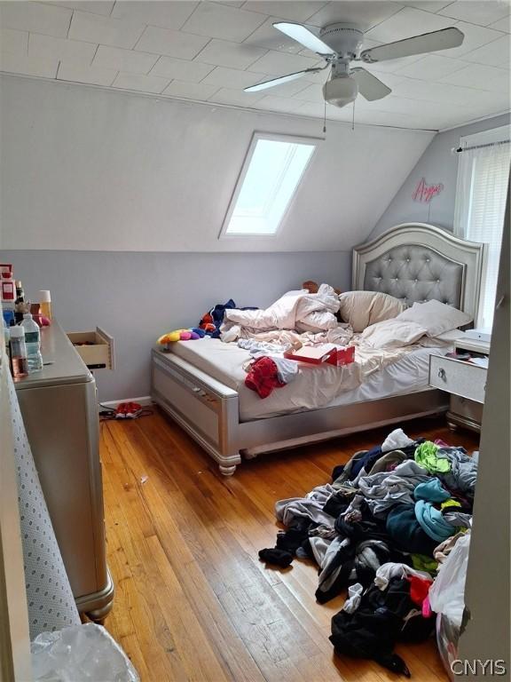 bedroom featuring ceiling fan, lofted ceiling with skylight, and light wood-type flooring