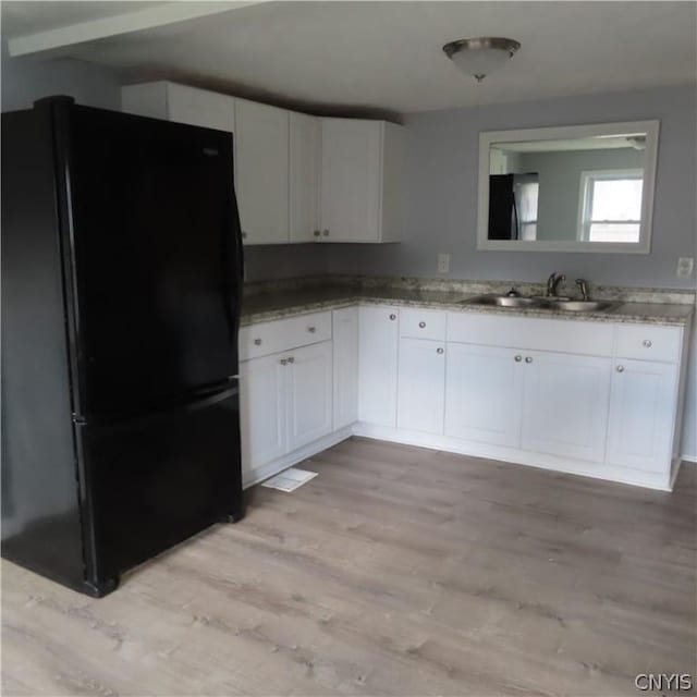 kitchen with light stone countertops, sink, black refrigerator, white cabinets, and light wood-type flooring