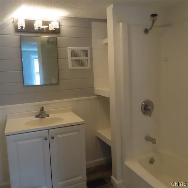 bathroom with a textured ceiling, vanity, shower / bath combination, and wooden walls