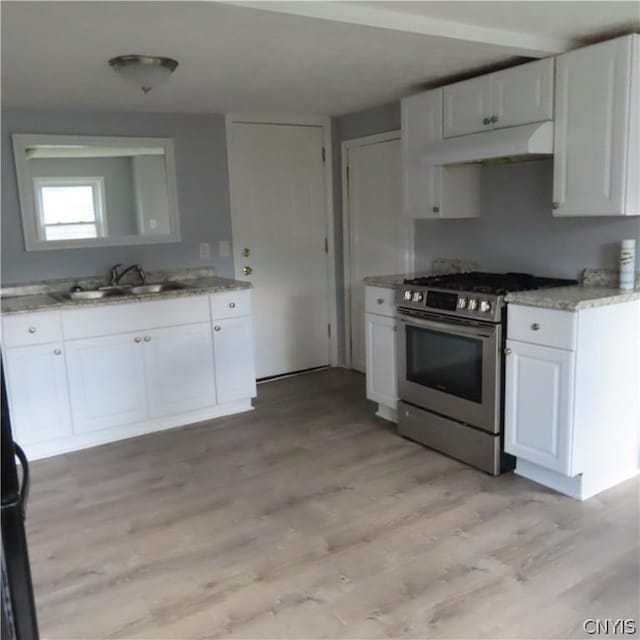 kitchen with sink, light stone counters, high end stainless steel range, white cabinets, and light wood-type flooring