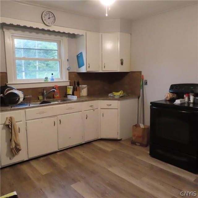 kitchen with light wood-type flooring, white cabinetry, black range with electric stovetop, and sink