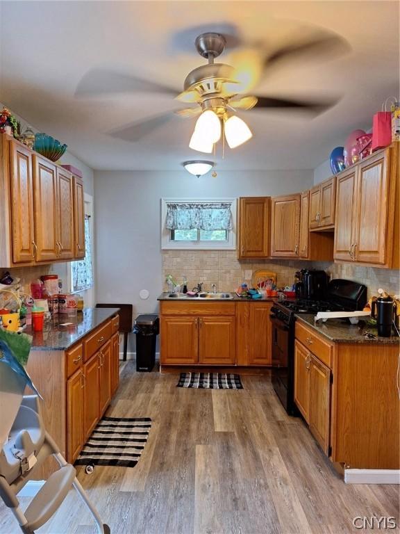 kitchen featuring gas stove, light hardwood / wood-style floors, dark stone counters, and a healthy amount of sunlight