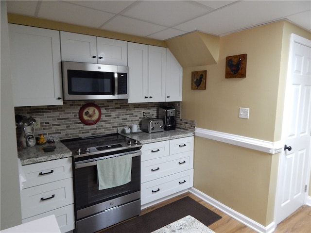 kitchen with tasteful backsplash, wood-type flooring, a paneled ceiling, white cabinets, and appliances with stainless steel finishes