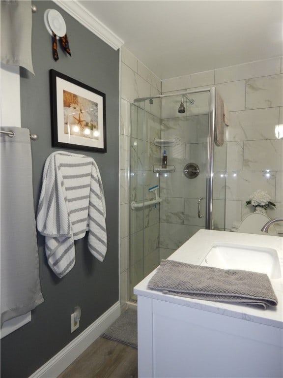 bathroom with a shower with shower door, wood-type flooring, vanity, and crown molding