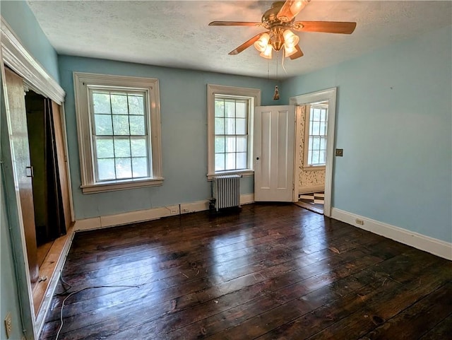 spare room featuring a wealth of natural light, radiator, dark wood-type flooring, and ceiling fan