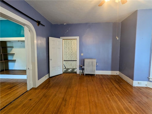 unfurnished bedroom with hardwood / wood-style floors, ceiling fan, radiator heating unit, and a closet