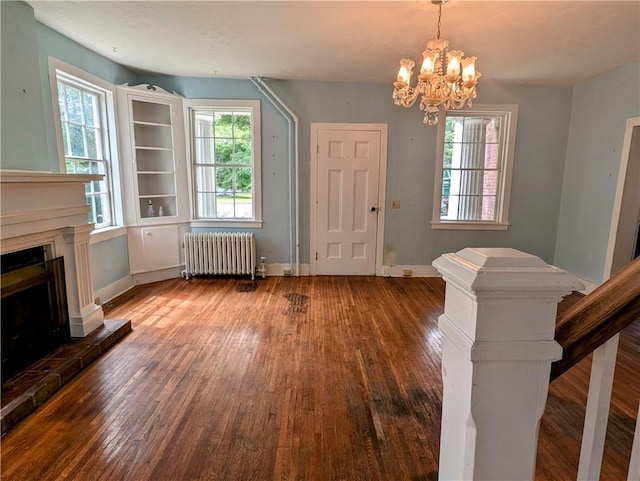 unfurnished living room with dark hardwood / wood-style floors, plenty of natural light, radiator, and an inviting chandelier