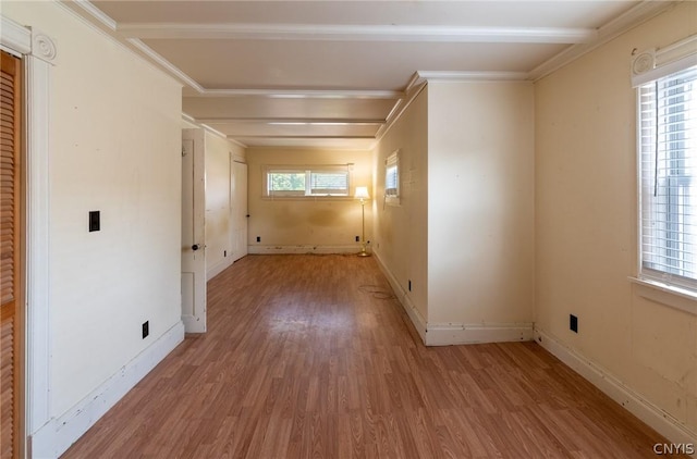 unfurnished room featuring beam ceiling, ornamental molding, a healthy amount of sunlight, and light wood-type flooring