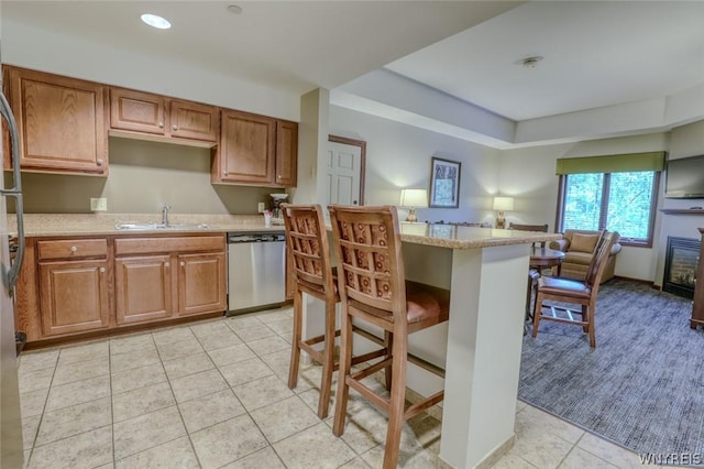 kitchen with sink, a breakfast bar, stainless steel dishwasher, and light tile patterned floors