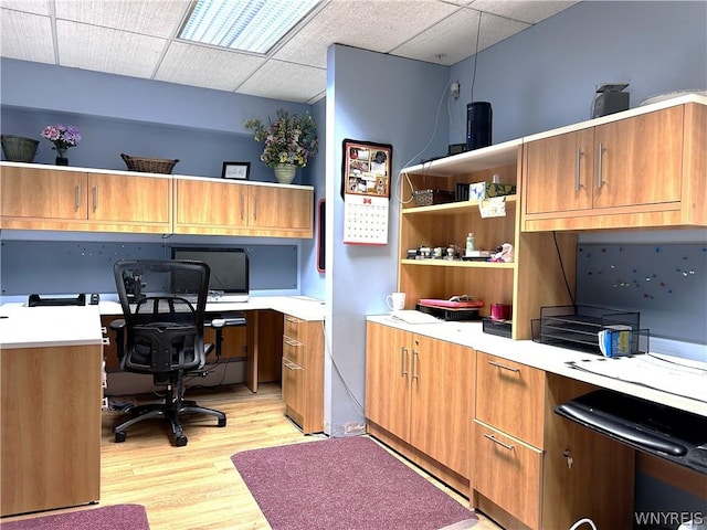 office with a paneled ceiling, built in desk, and light wood-type flooring