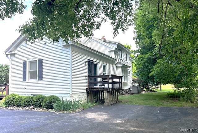 view of side of property featuring central AC, a lawn, and a wooden deck