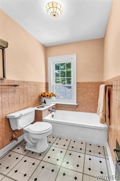 bathroom with tile walls, a tub to relax in, and toilet