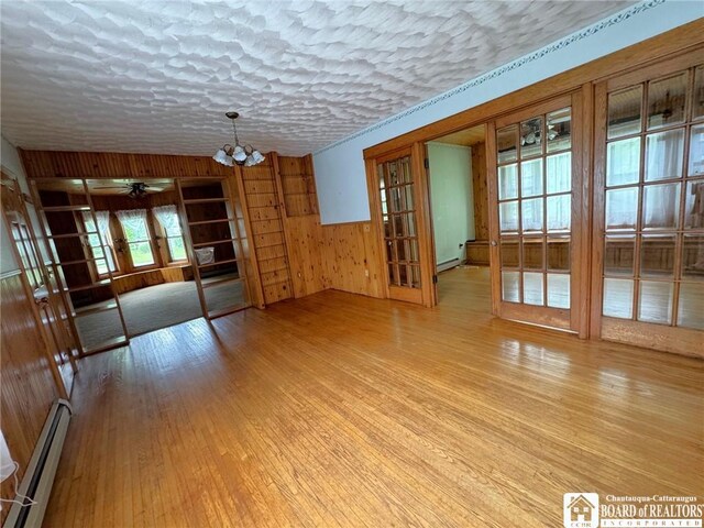 unfurnished living room with wood walls, light hardwood / wood-style floors, french doors, and baseboard heating