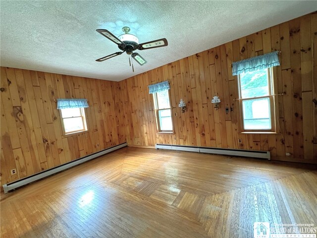 spare room featuring a textured ceiling, baseboard heating, and wood walls