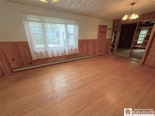 empty room featuring baseboard heating, wood-type flooring, a textured ceiling, and a notable chandelier