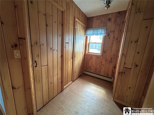 interior space with baseboard heating, a textured ceiling, and wood walls