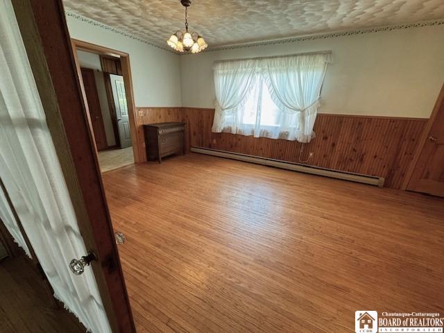 unfurnished dining area featuring hardwood / wood-style floors, a notable chandelier, a baseboard radiator, and a textured ceiling