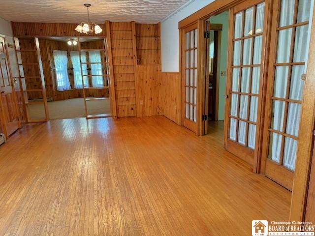 spare room featuring light hardwood / wood-style flooring, french doors, a chandelier, and wood walls