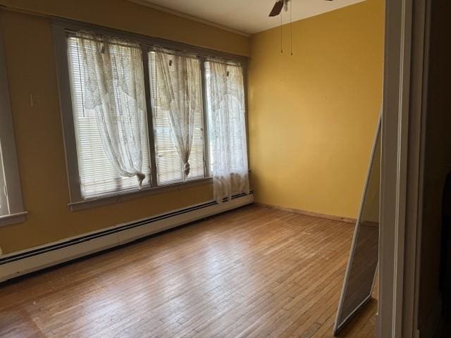 empty room with a baseboard heating unit, a ceiling fan, and wood finished floors