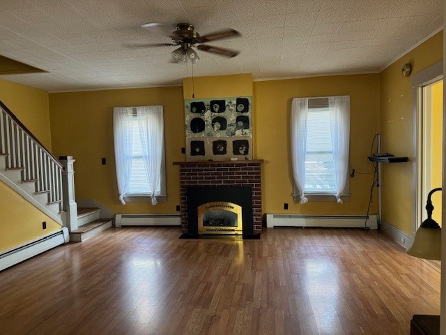 unfurnished living room featuring hardwood / wood-style flooring, a brick fireplace, a baseboard heating unit, and ceiling fan