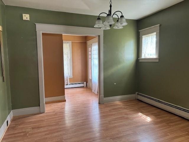 spare room featuring a baseboard heating unit, baseboards, light wood-style floors, and a chandelier