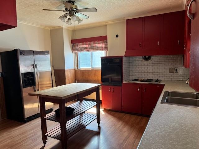 kitchen featuring oven, a wainscoted wall, stainless steel fridge, red cabinets, and cooktop