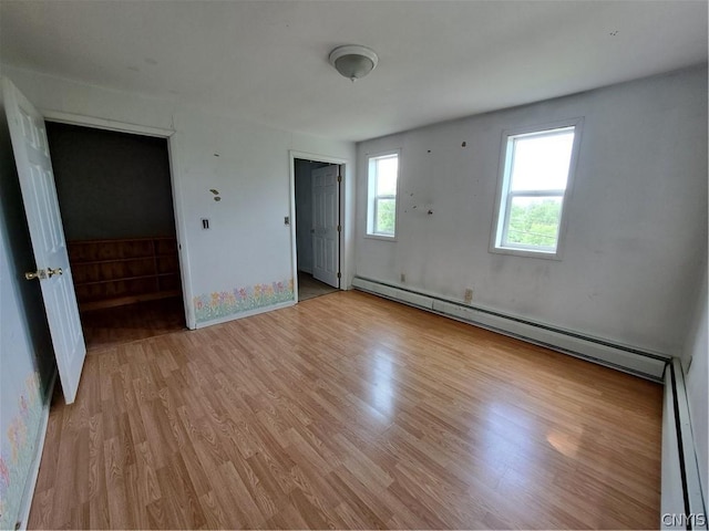 unfurnished bedroom featuring light wood-type flooring, a baseboard radiator, and multiple windows