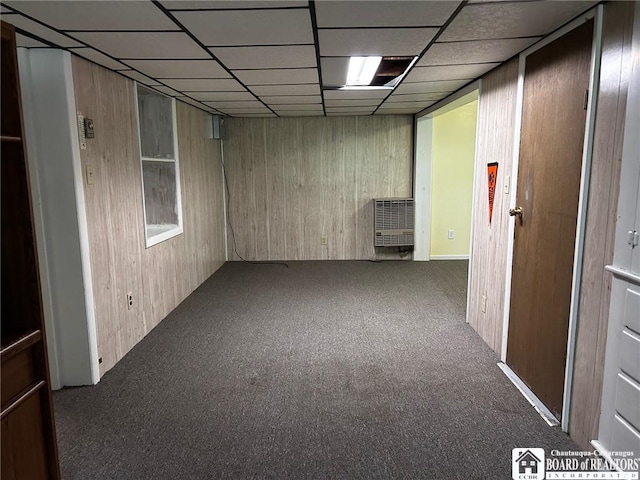 carpeted spare room with wooden walls, heating unit, and a drop ceiling