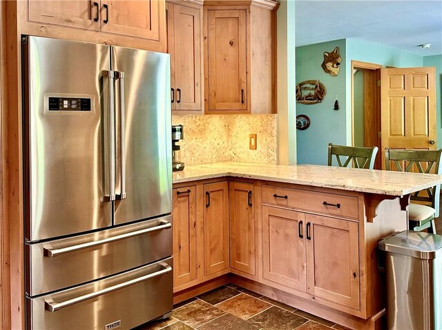 kitchen with decorative backsplash, kitchen peninsula, light stone countertops, a breakfast bar area, and high quality fridge